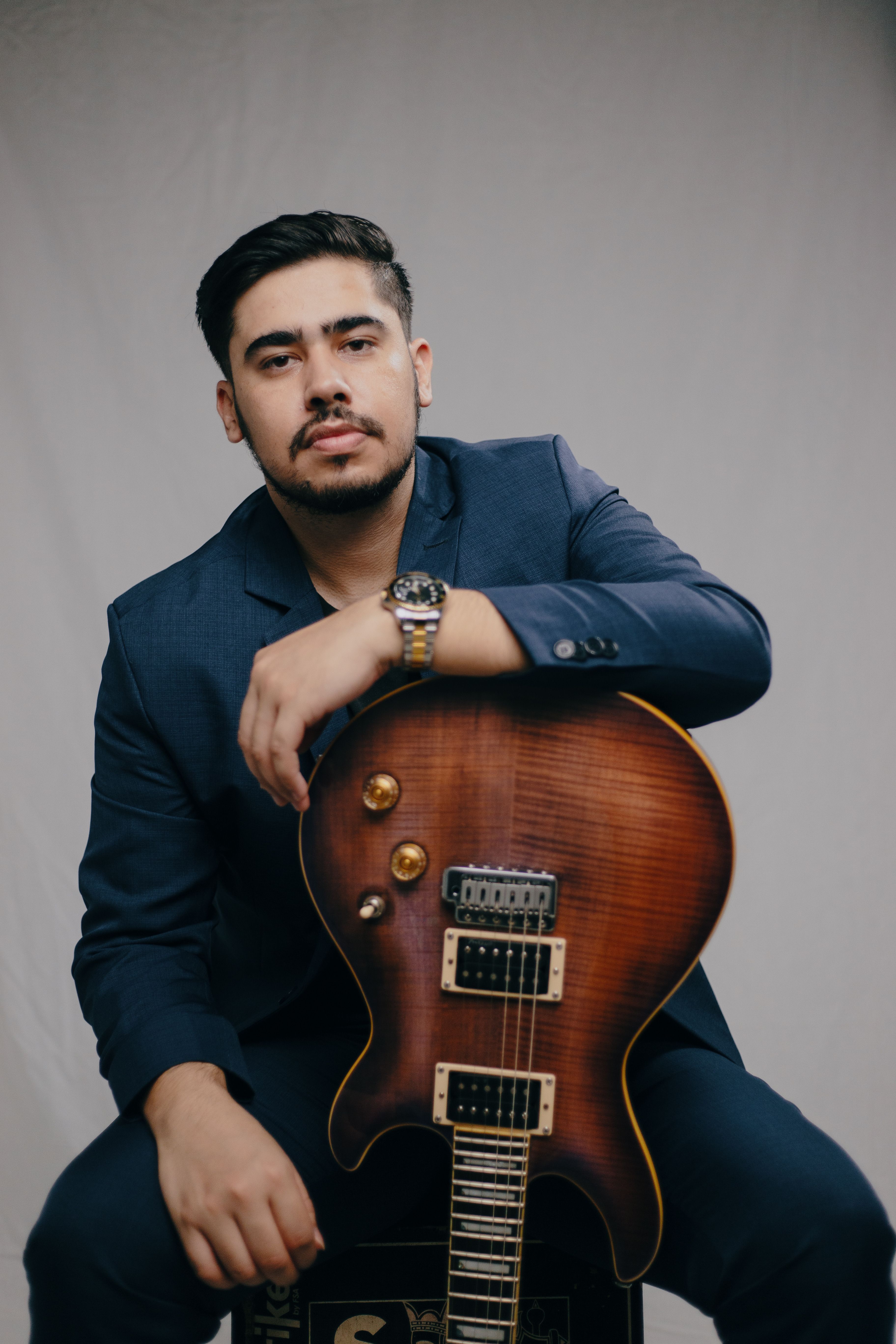 Stylish man holding an electric guitar, posing for a portrait on a gray background.