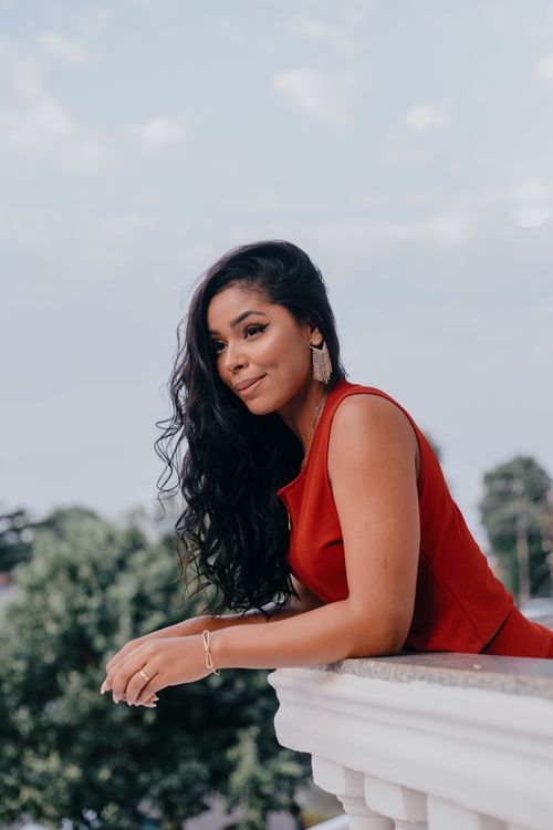 Free Stylish woman in red dress leans on balcony with graceful poise outdoors. Stock Photo