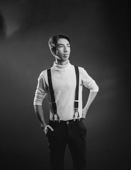 Stylish black and white portrait of a man in suspenders posing confidently in studio lighting.