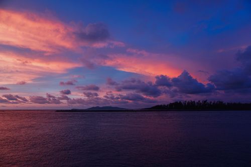Free Stunning sunset with vibrant clouds over a tranquil ocean, creating a dramatic and serene landscape. Stock Photo