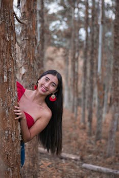 Smiling woman in red dress peeking from behind a tree in a forest in San Agustín, Colombia.