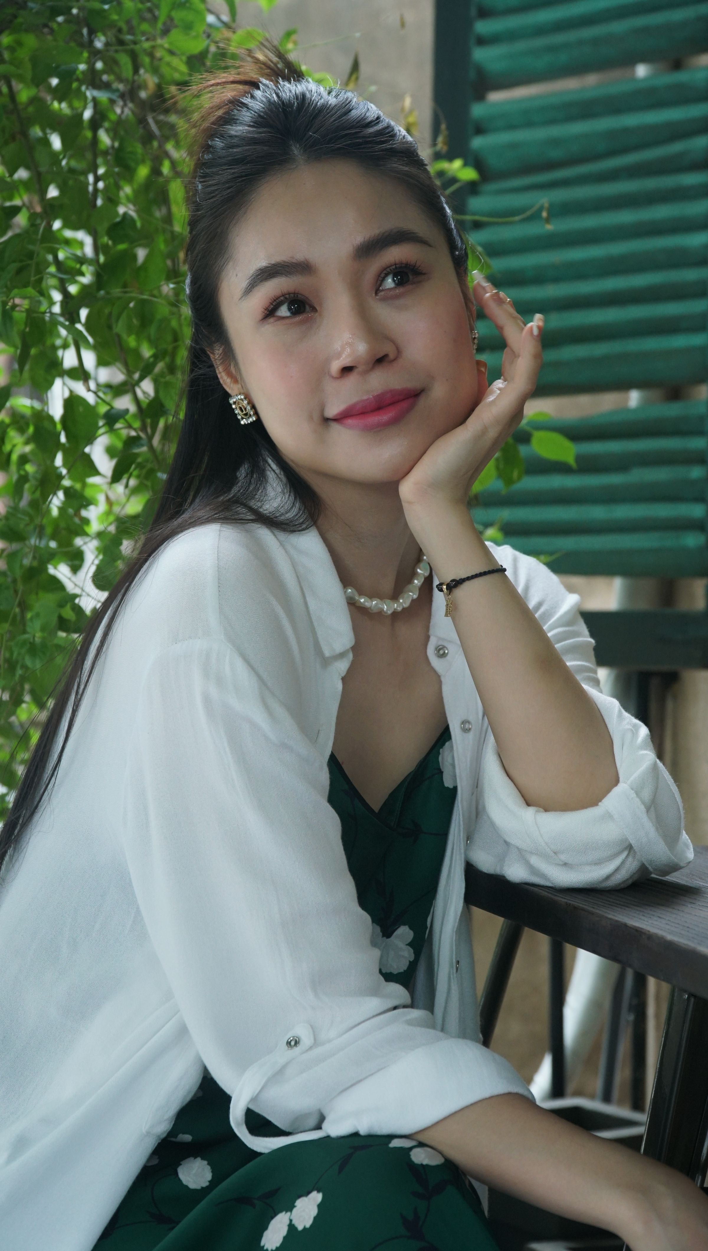 A woman in a white shirt and floral dress sitting outdoors, showcasing elegance and a relaxed mood.