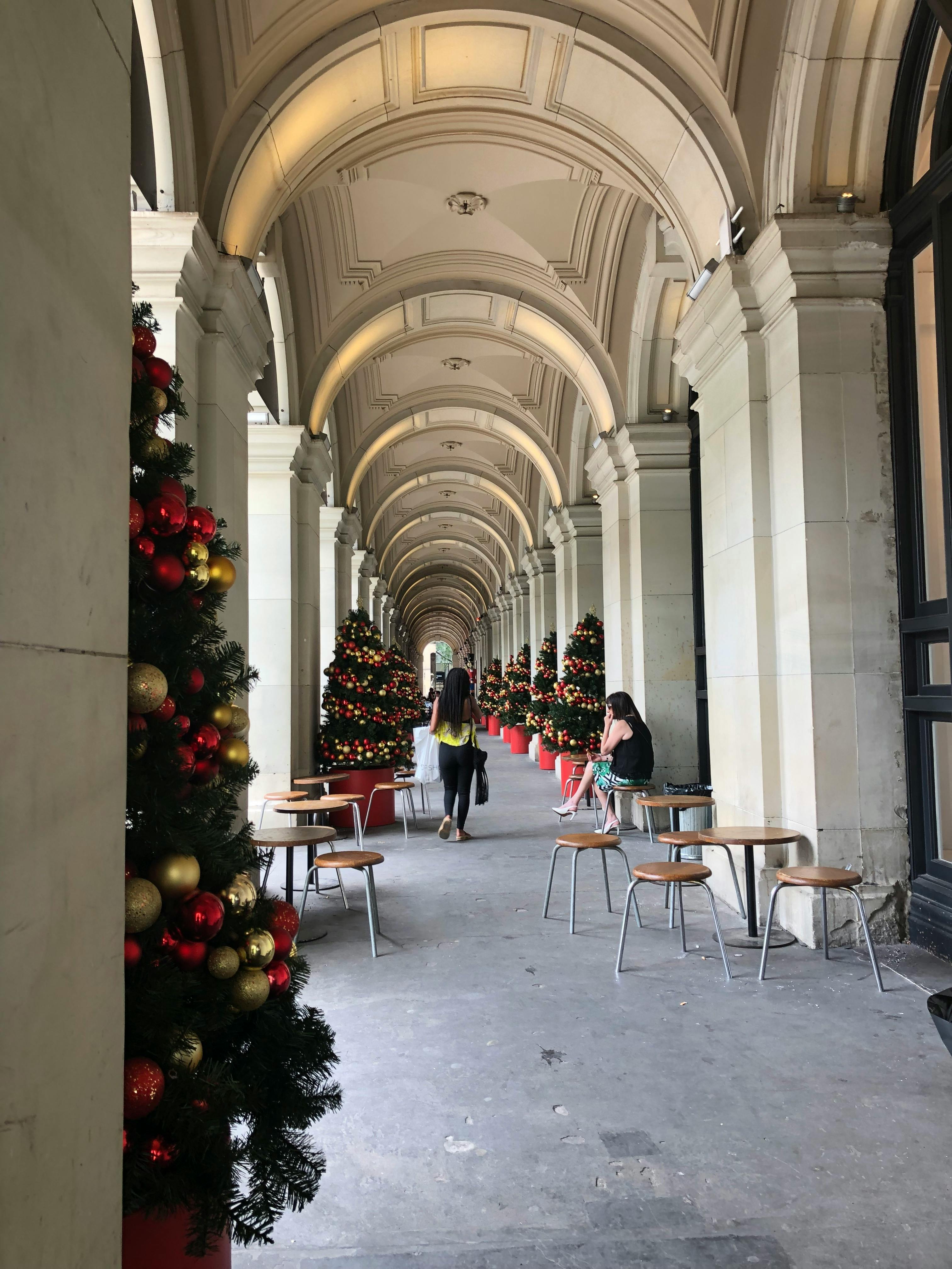 室内拱形走廊装饰着圣诞饰品并设有座位，以节日树木和人群为特色