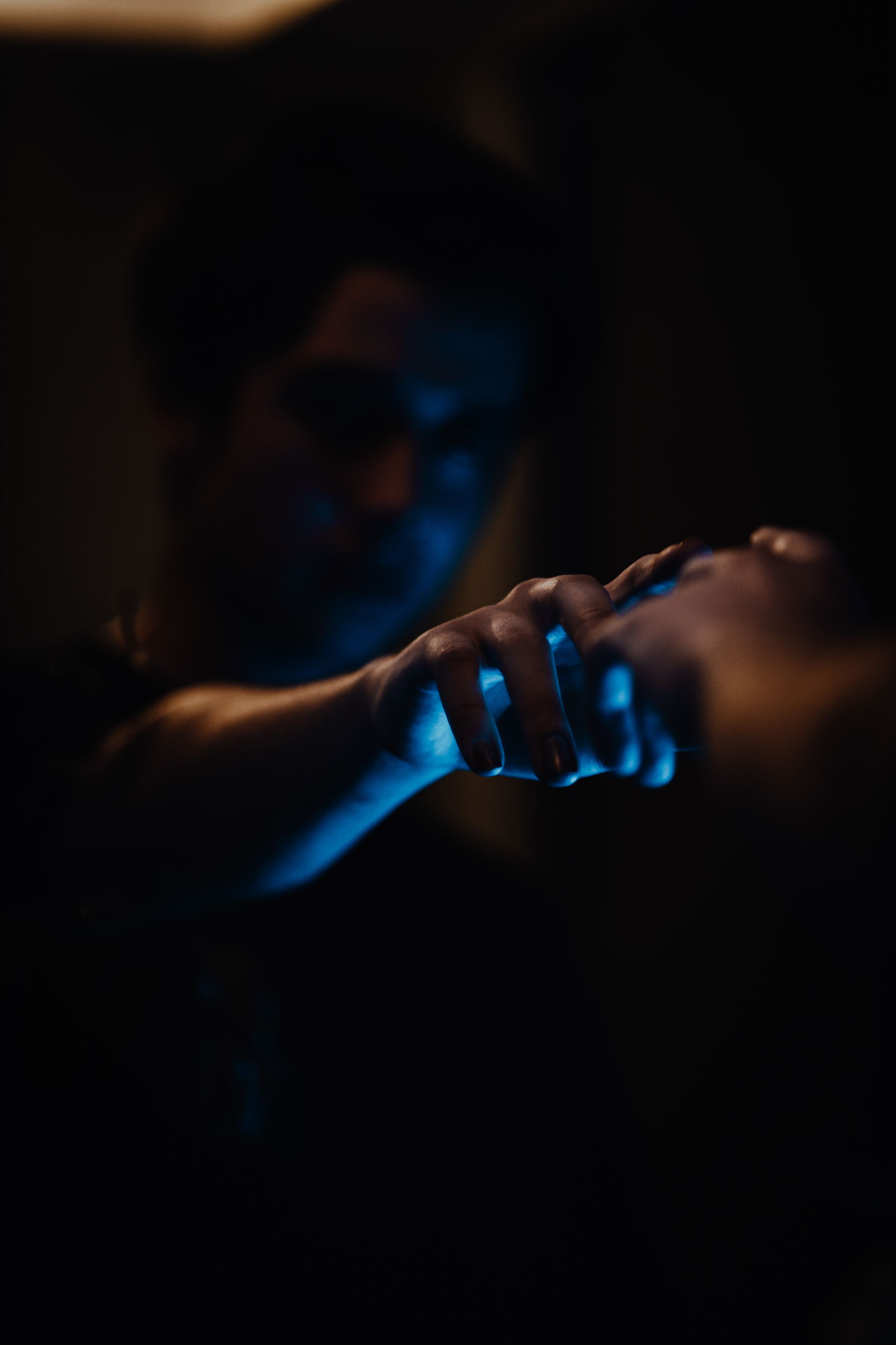 Two human hands meeting in a dark environment illuminated by deep blue light.