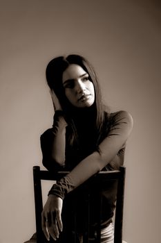 Dramatic sepia portrait of a woman sitting pensively on a chair.