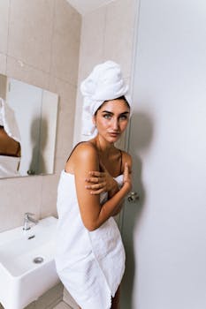 A woman wrapped in a white towel stands near a sink in a modern bathroom.