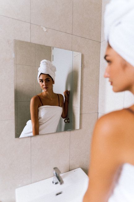 Woman wrapped in towel gazing at her reflection in the bathroom mirror.
