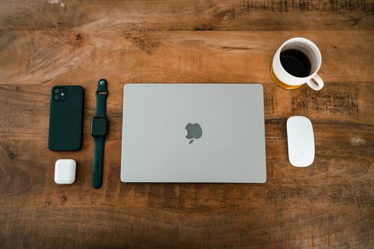Flat lay image featuring a laptop, smartphone, smartwatch, wireless earbuds, and coffee cup on a wooden desk.