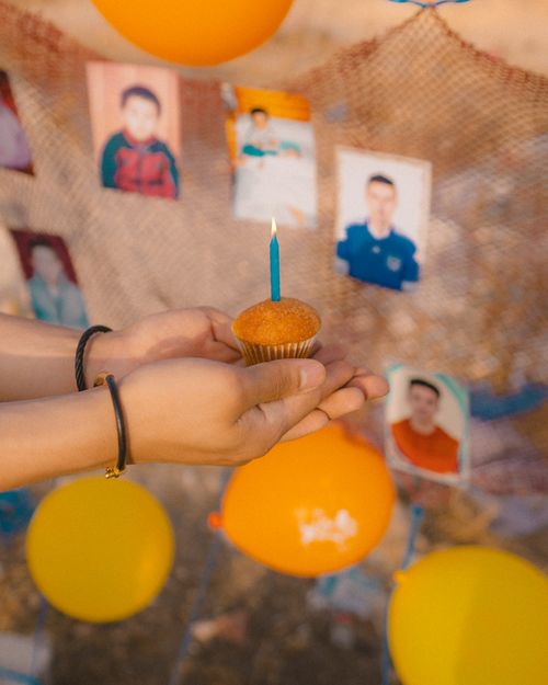 Free Close-up of hands holding a cupcake with a lit candle, set against a backdrop of photos and balloons. Stock Photo