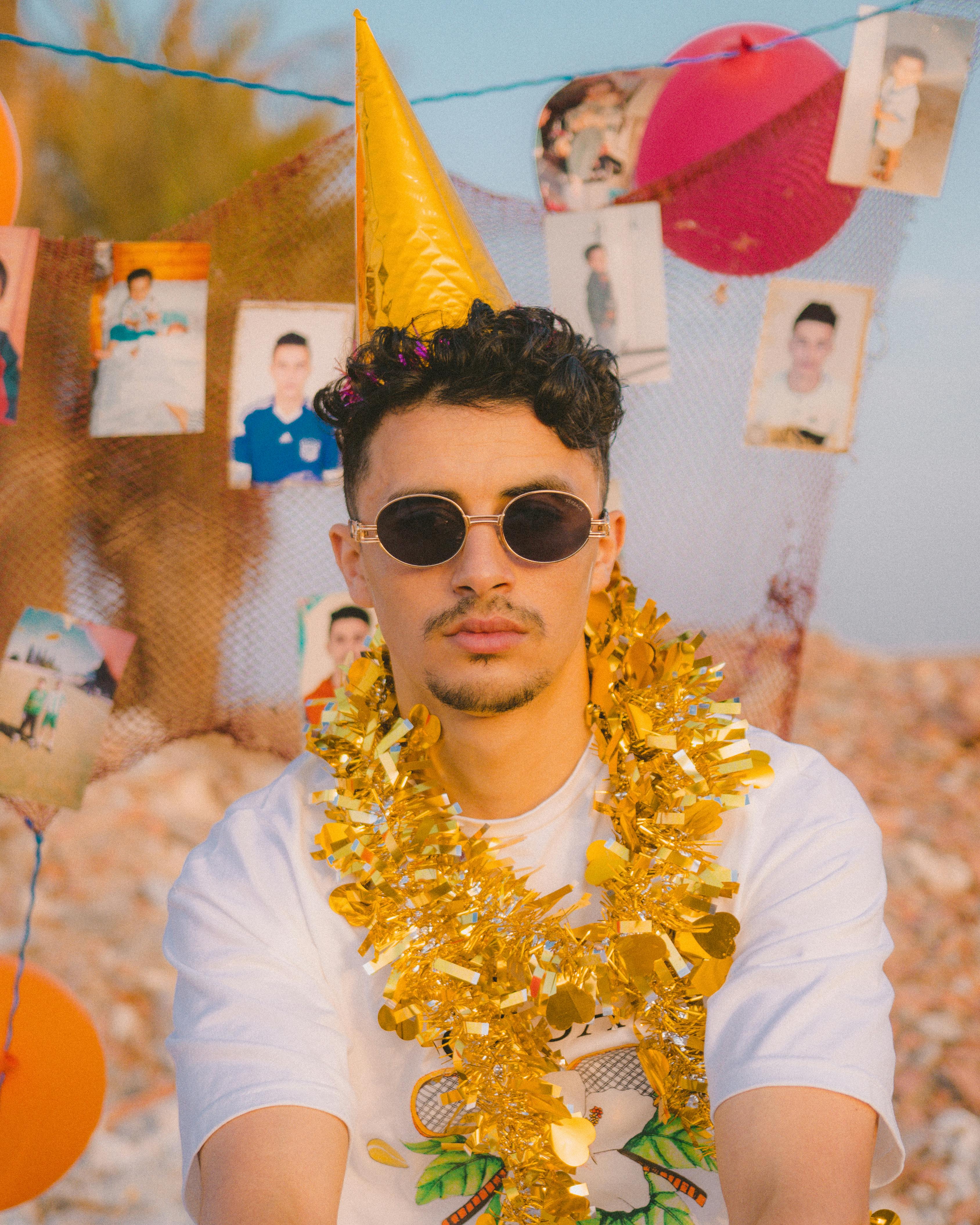 Man in party hat and sunglasses with garland enjoying a birthday celebration outdoors.