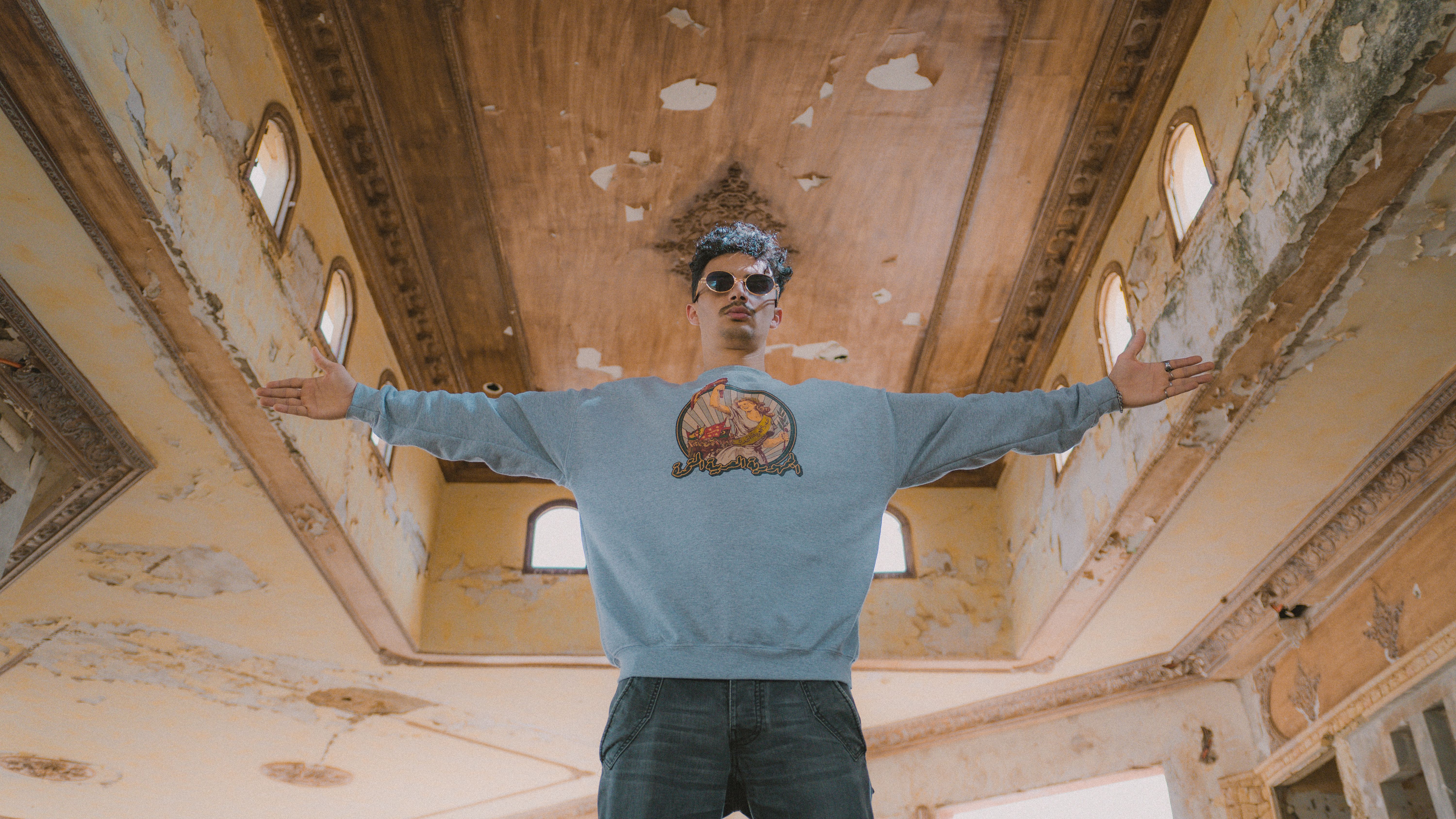 Stylish young man stands in an abandoned building, embracing freedom with arms outstretched.