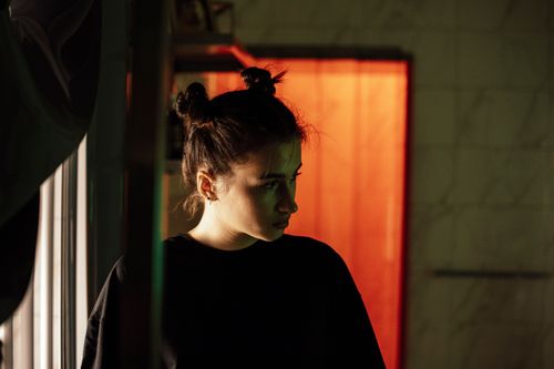 Free A woman stands indoors in a moody setting with dramatic lighting and shadows. Stock Photo