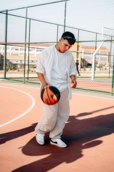 Casual young man poses with basketball on an outdoor court, showcasing stylish sports fashion.