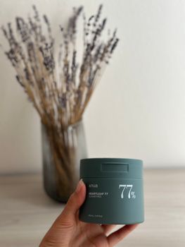 Hand holding a skincare product jar with dried lavender decor in the background.