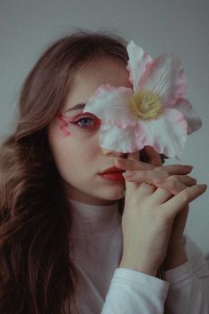 A young woman with creative makeup poses holding a large flower.