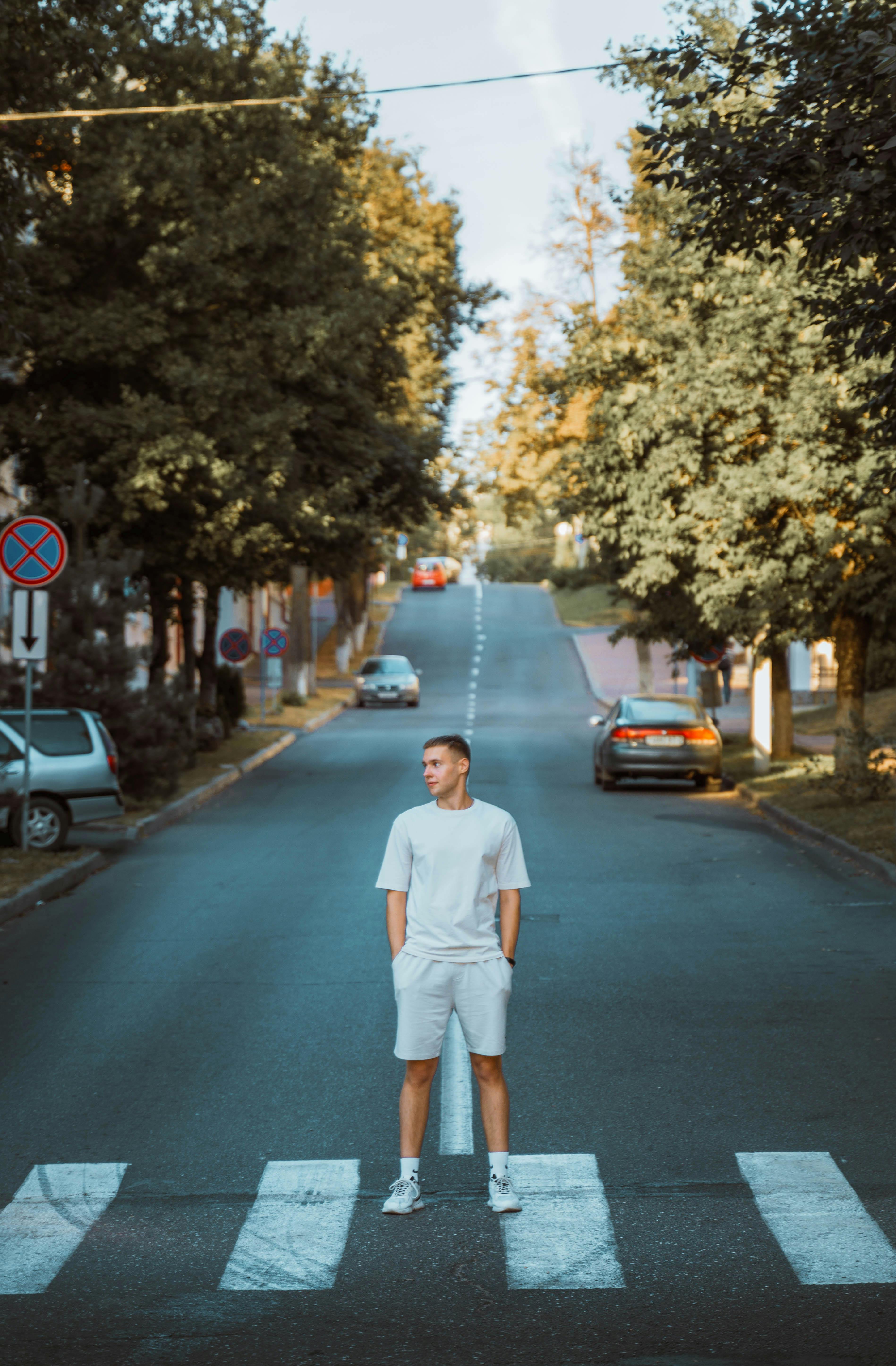 a full length portrait of a guy in light colored clothes in the middle of a road in the city