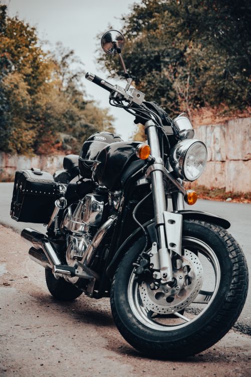 Free Close-up of a black motorcycle parked on a rural road surrounded by trees. Stock Photo
