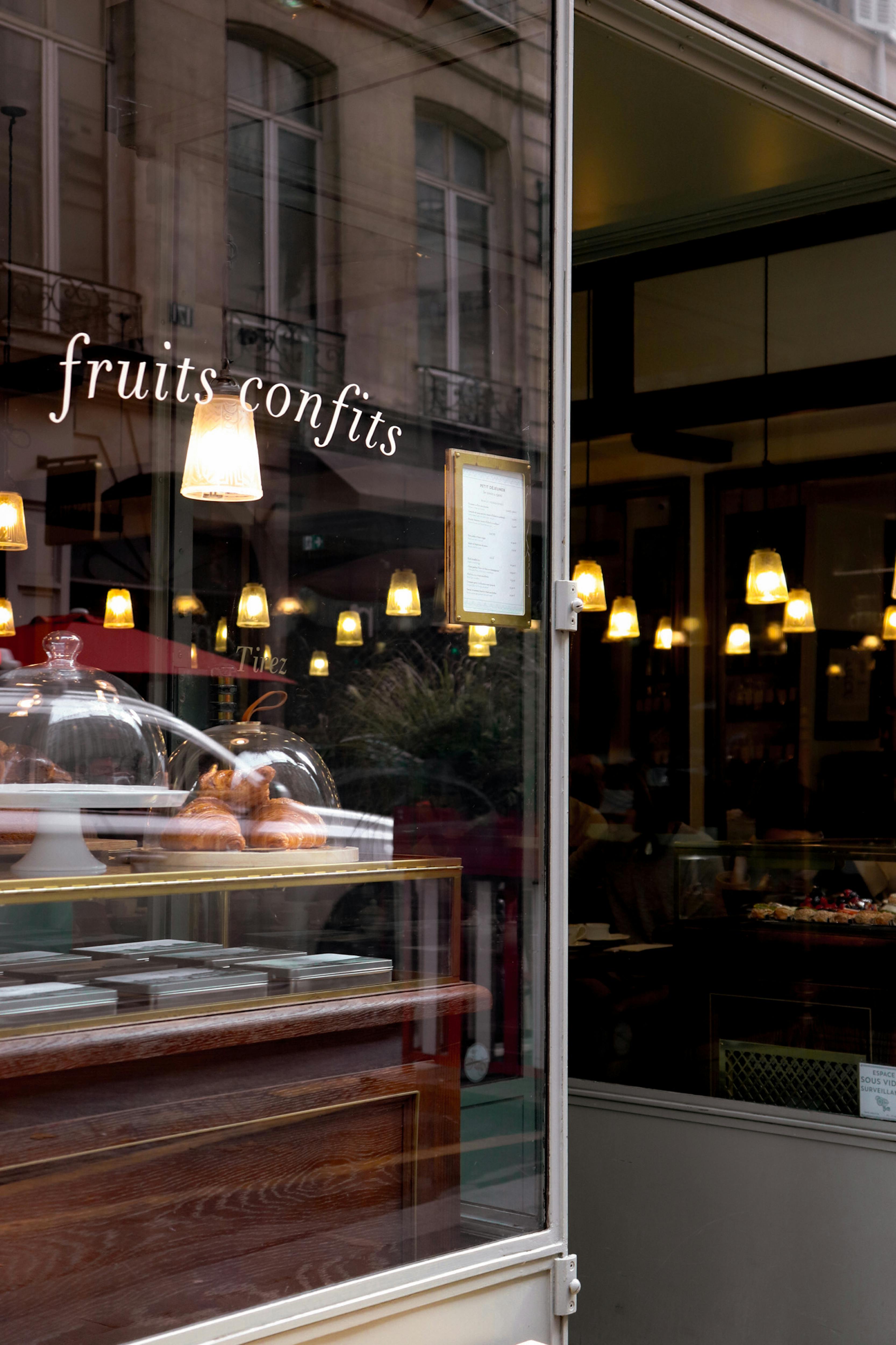 Charming Parisian bakery storefront showcasing "fruits confits" with warm lighting reflections.