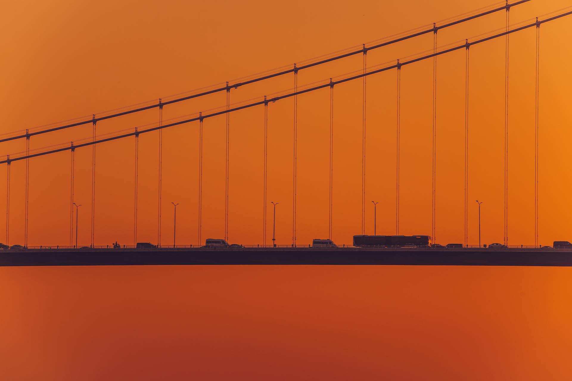 Silhouette of the Fatih Sultan Mehmet Bridge in Istanbul against a vibrant sunset sky.