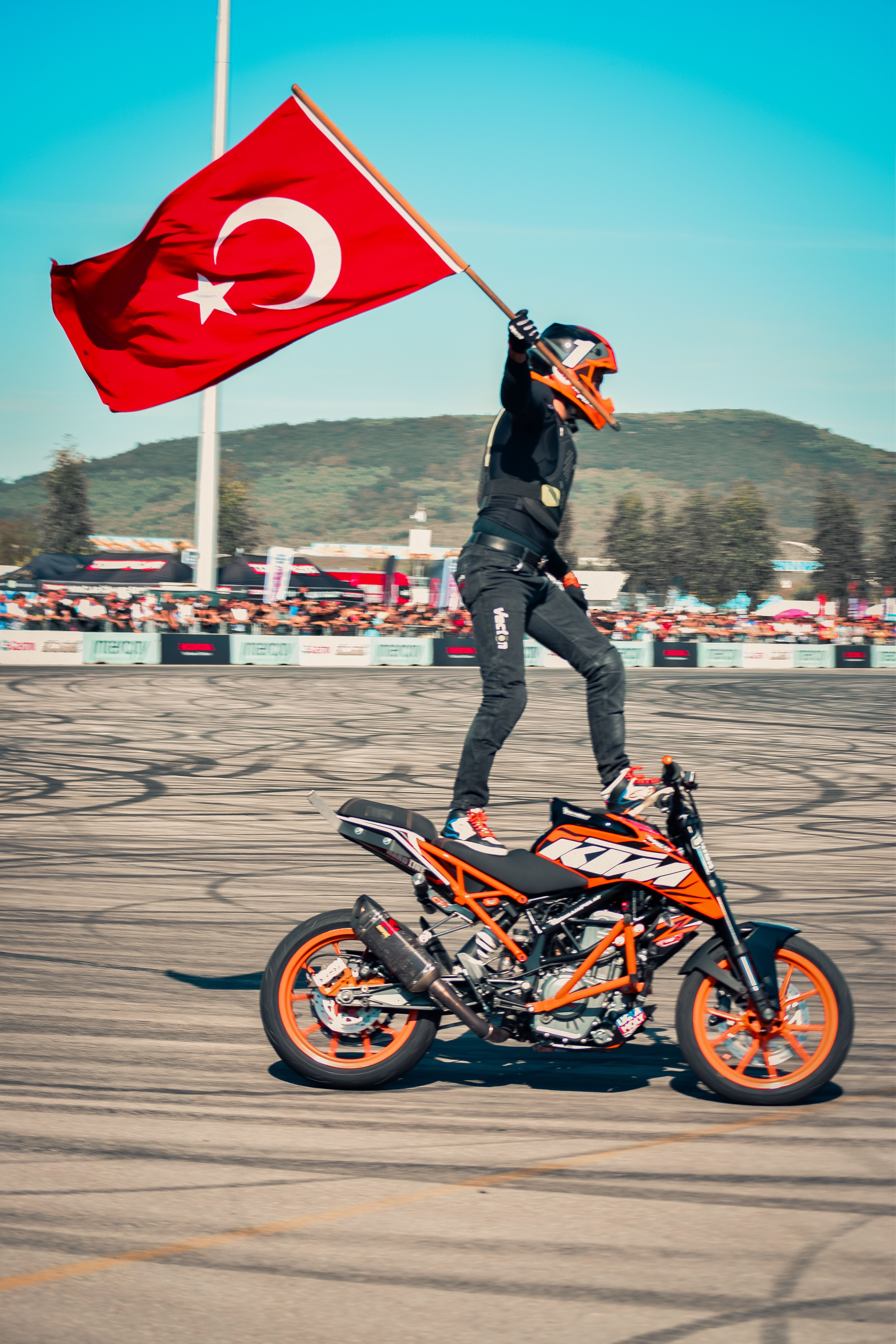 Motorcyclist performing a stunt with Turkish flag at an outdoor event.