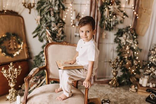 Little Boy in White Shirt Sitting on Armchair with Book in Hand