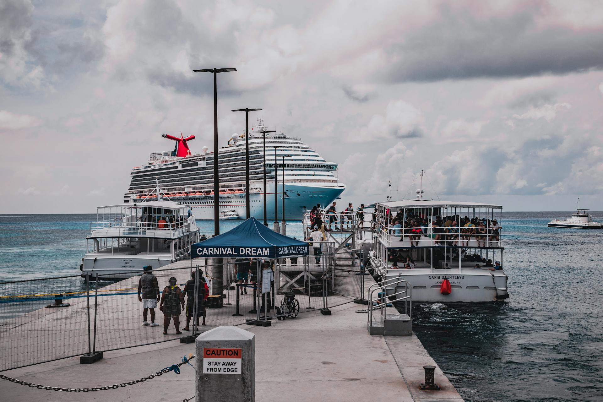Large cruise ship docked at a scenic Caribbean port with passengers boarding nearby boats.