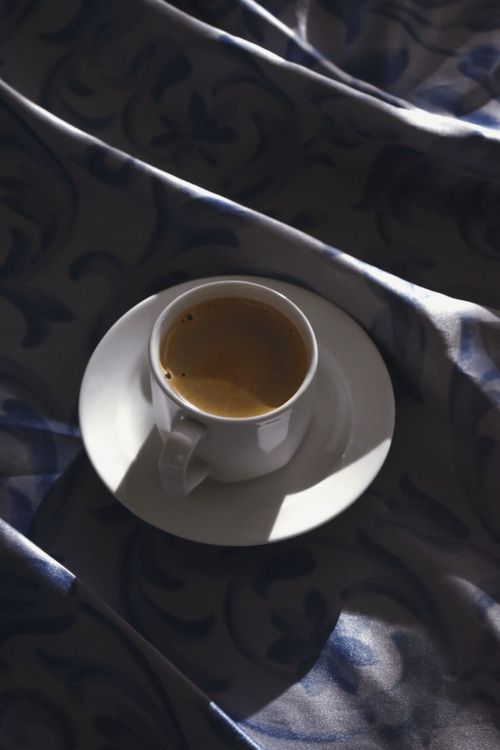 Free A white coffee cup on patterned fabric in sunlight, capturing a tranquil morning vibe. Stock Photo