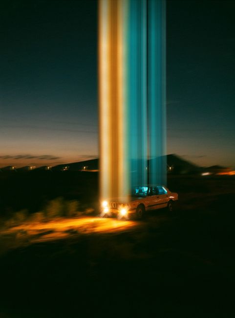 A surreal view of a classic car under beams of light in the Baku desert at sunset.