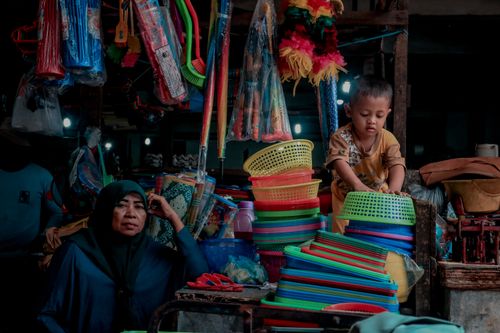 Free A mother with her child at a colorful market stall filled with plastic goods. Stock Photo