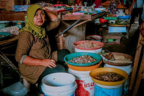 Free Woman in green hijab managing a seafood stall at an Indonesian market, displaying various dishes. Stock Photo