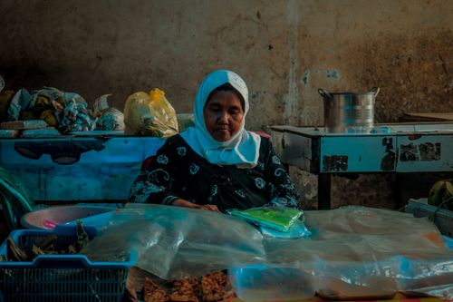 Free A woman working at an indoor market stall with packaged goods on display. Stock Photo