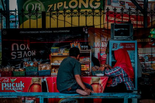 Free A vibrant market stall in Indonesia selling snacks, captured from behind with two people. Stock Photo