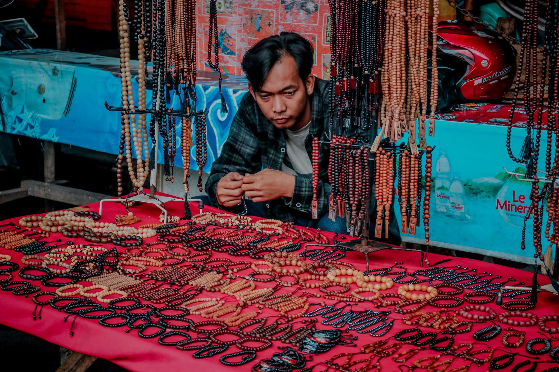 Man selling handmade beaded bracelets and necklaces at a vibrant urban market stall.