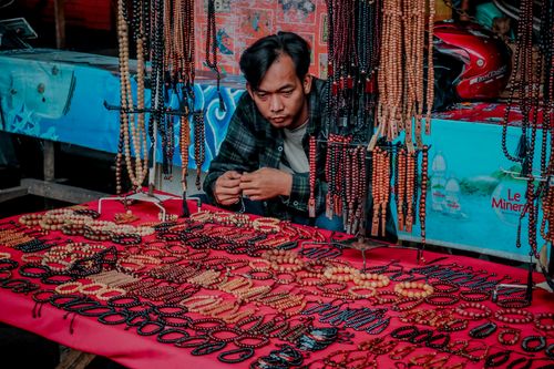 Free Man selling handmade beaded bracelets and necklaces at a vibrant urban market stall. Stock Photo