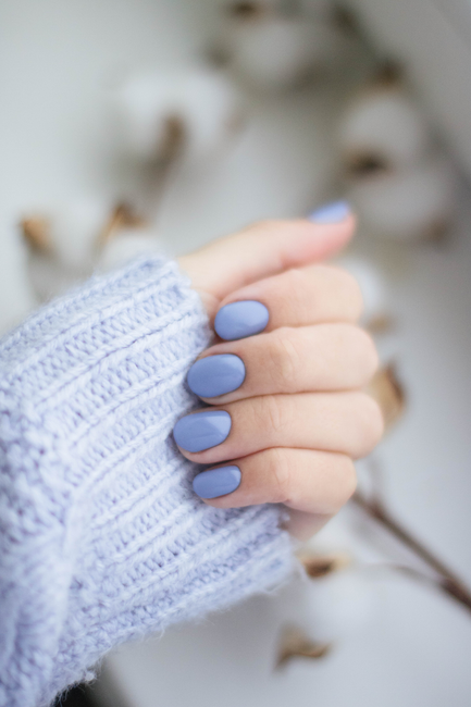Fotomural Un primer plano de la mano de una mujer con uñas púrpuras y tejido de punto, mostrando moda trendy.