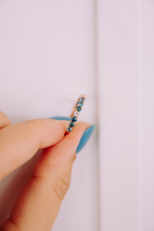 Gold ring with precious stones in woman hand with blue manicure against white wall