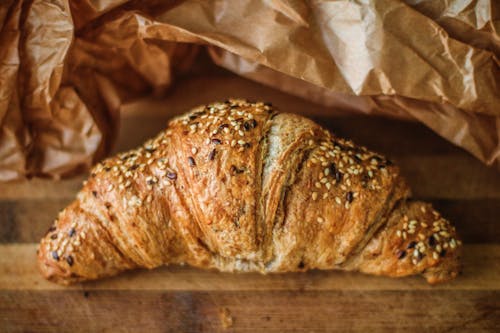 Top view of delicious crispy croissant with sesame seeds on wooden table near paper bag