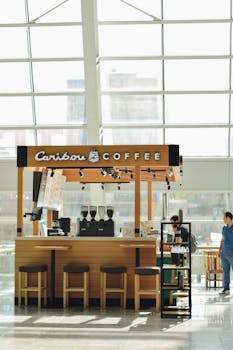 Cozy coffee stall in a bustling airport with natural lighting and bar seating.