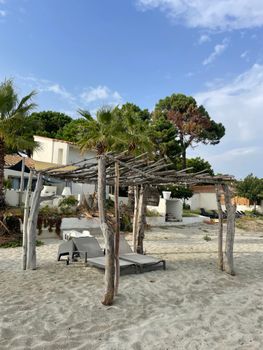 Relaxing beach scene with sun loungers under a rustic pergola on a sandy shore.