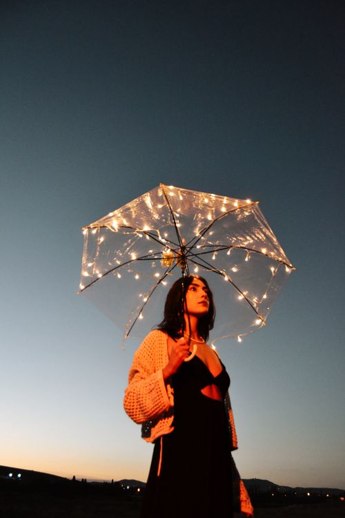 Free A woman holding a string-lit umbrella against a twilight sky, creating a magical and serene atmosphere. Stock Photo