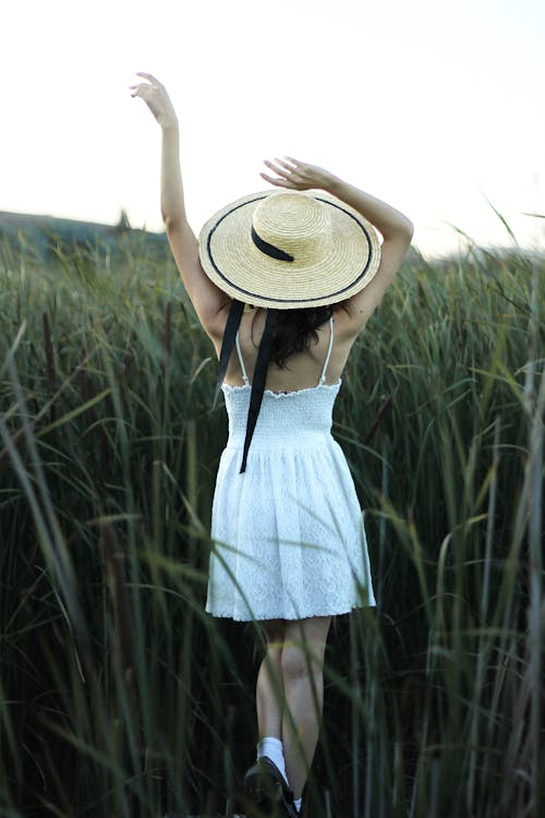 Back View of a Woman in a White Dress Walking on a Grass Field