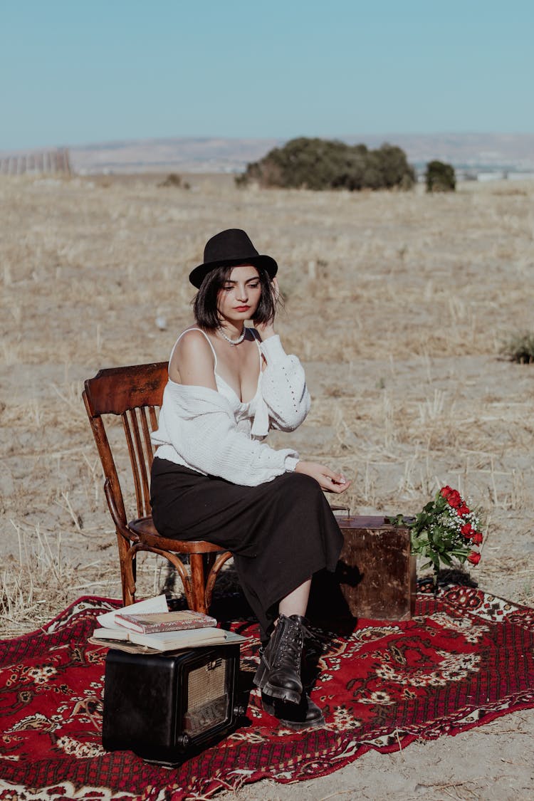 Woman In Hat Posing On Chair On Carpet On Field