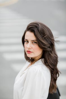 Stylish woman with brunette hair posing confidently in Baku on an urban crosswalk.