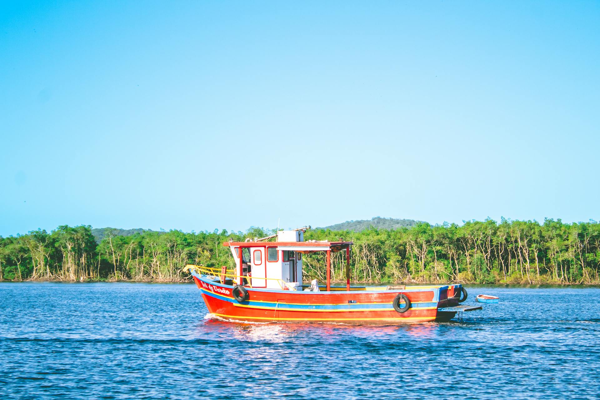 A vibrant fishing boat floats on Paranaguá Bay, Brazil, under a clear blue sky.