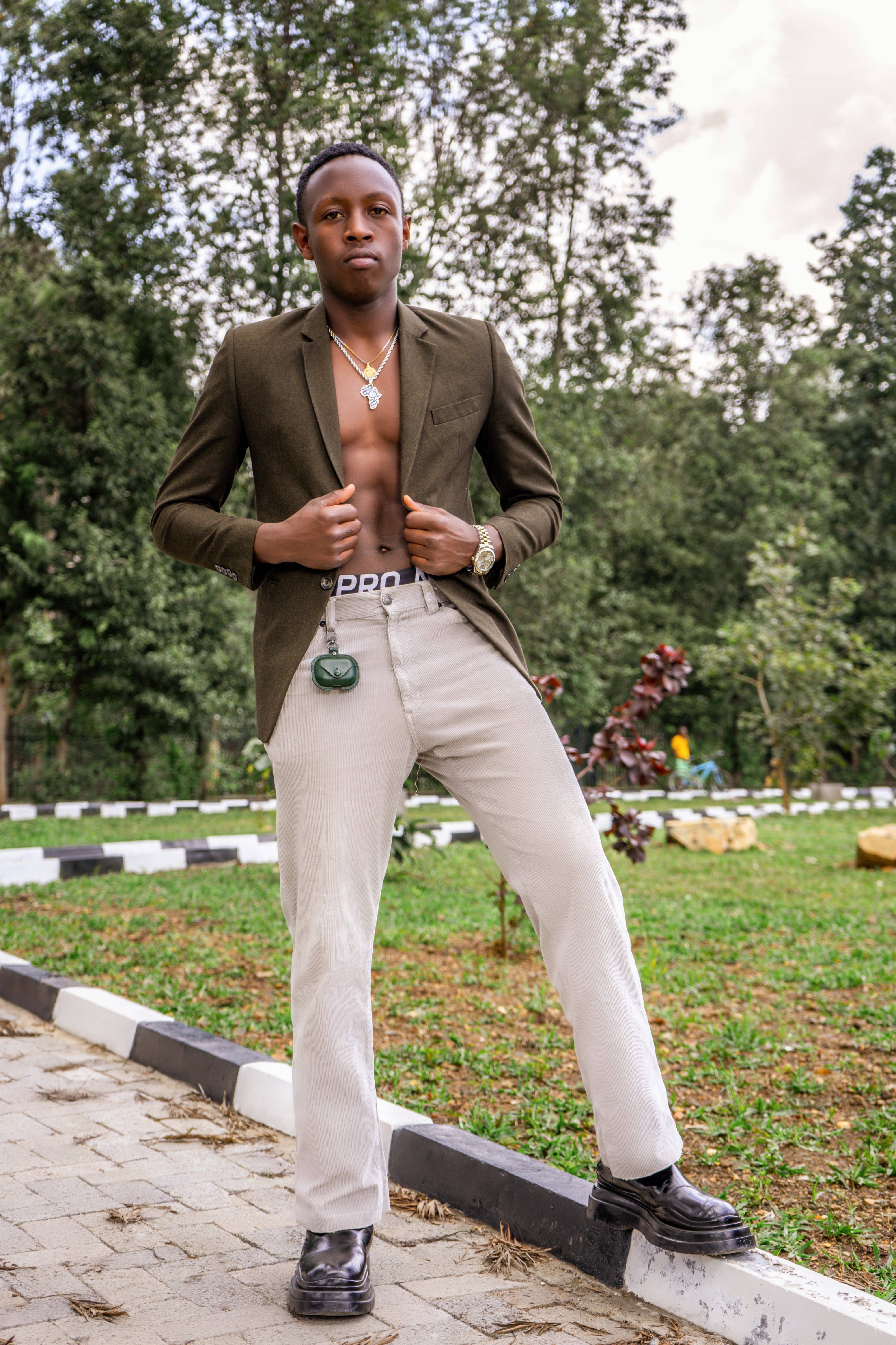 A young man poses confidently in an outdoor park wearing a blazer and light trousers, embracing modern fashion.