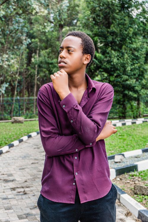 Free A thoughtful young man in a purple shirt posing at a park on a sunny day. Stock Photo