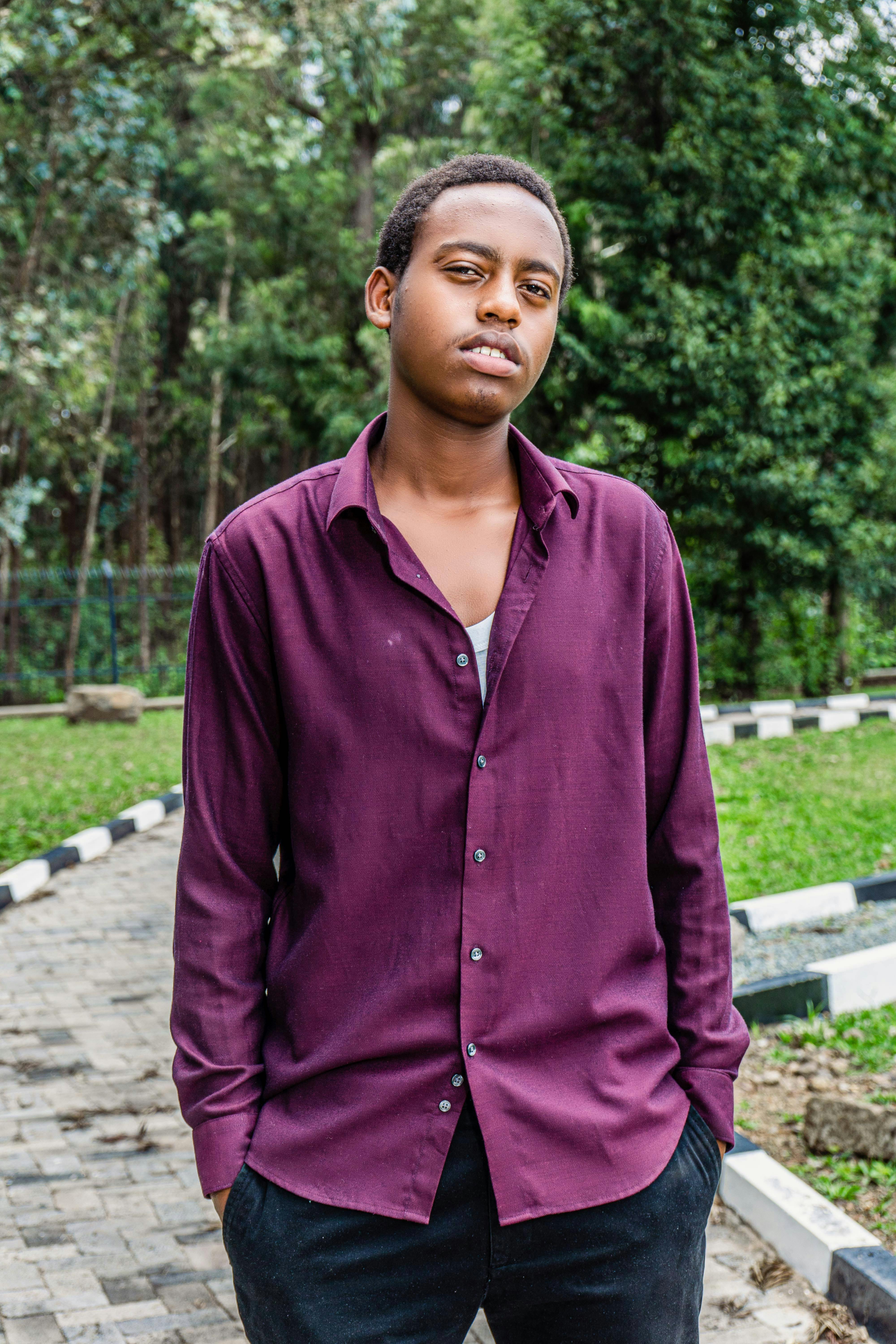 Fashionable young man in a purple shirt posing outdoors in a peaceful park setting.