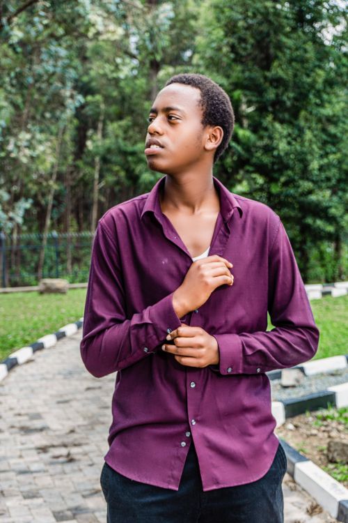 Free Portrait of a young man in a burgundy shirt posing in a scenic park setting. Stock Photo