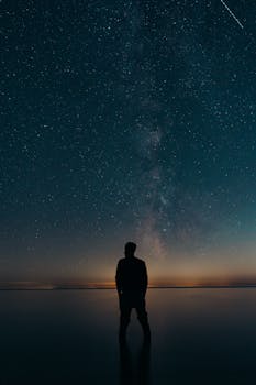 Silhouette of a person standing under a stunning starry sky with the Milky Way galaxy shining brightly.