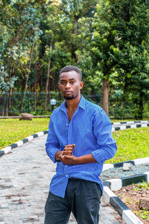 Free Man in a blue striped shirt posing confidently in an outdoor park setting. Stock Photo